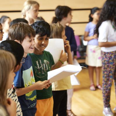 Three boys laugh whilst holding out a song sheet
